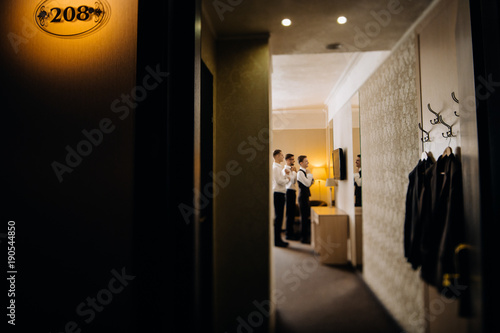 stylish groomsmen helping happy groom getting ready in the morning for wedding ceremony. luxury man in suit in room.