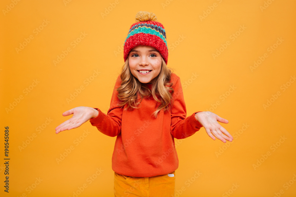 Smiling Young girl in sweater and hat shrugs her shoulders