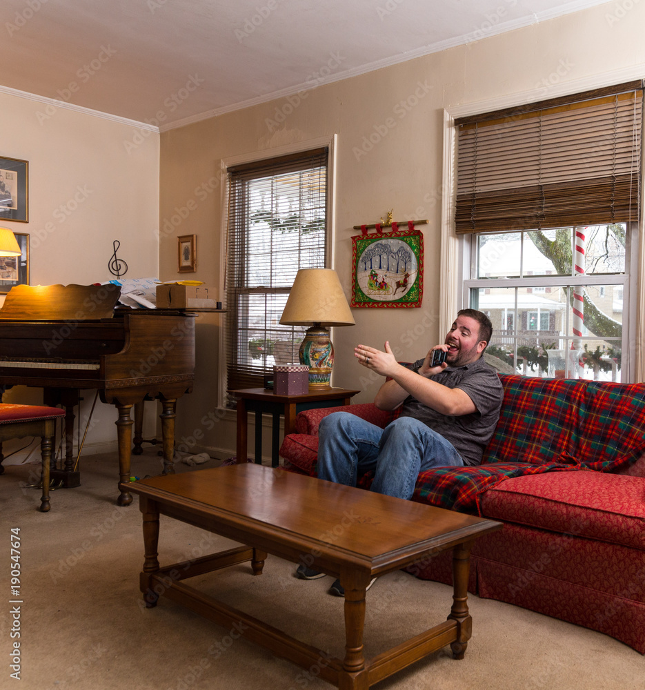 Obraz premium Young Caucasian Man Singing Karaoke Into His Phone While Sitting Alone In His Livingroom