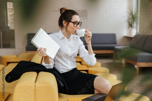 Young amazing business lady writing notes drinking coffee.