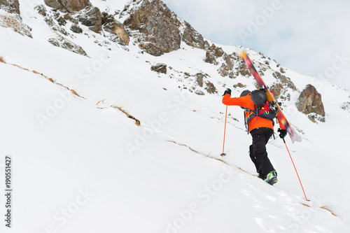 the ski freerider climbs the slope into deep snow powder with the equipment on the back fixed on the backpack.