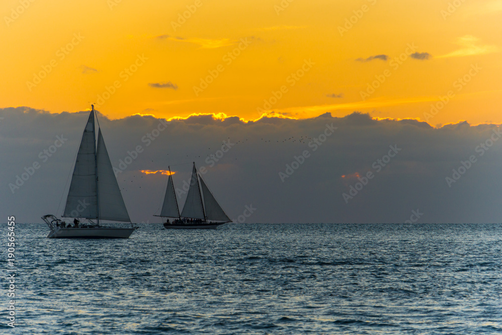 USA, Florida, Orange sunset behind clouds at key west with two sailing boats on the water
