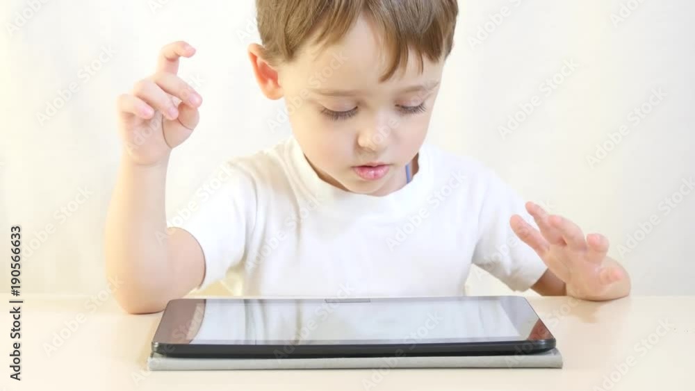 The child is sitting at the table and playing on the tablet. The child is sitting at the table and playing on the tablet.