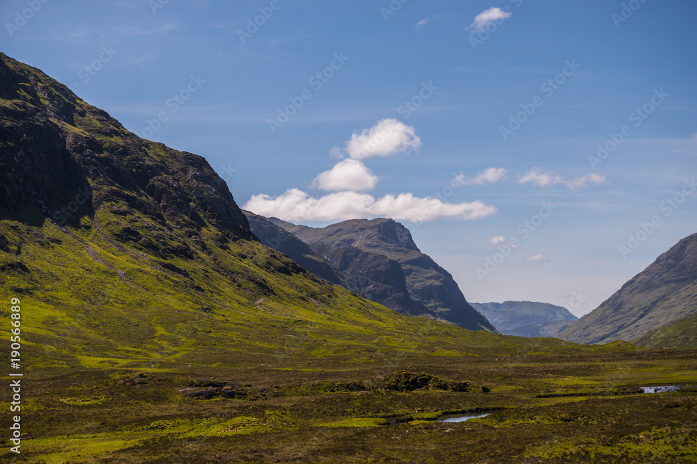 Naklejka premium Mountain landscape in the Glencoe area in Scotland, Springtime view mountains with grassland and countryside road in the valley of the Scottish highland near Glencoe