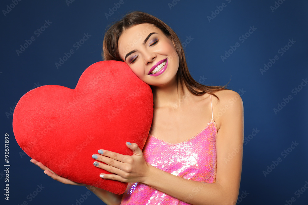 Romantic young woman with heart-shaped pillow on color background