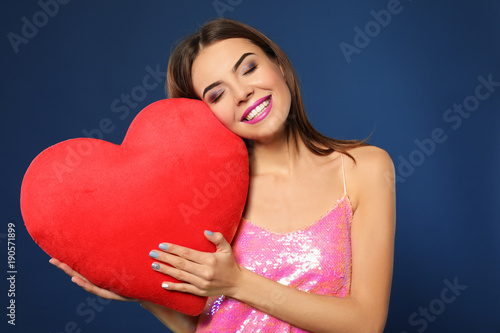 Romantic young woman with heart-shaped pillow on color background