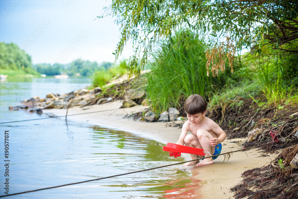 Fototapeta premium Baby boy playing with ship toy at sea. Child os on vacation in summer at the beach on vacations
