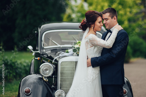 stylish bride and groom sensually posing near retro car with boh