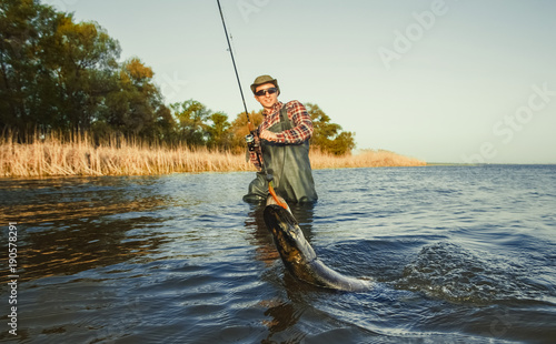 The fisherman is holding a fish pike caught on a hook in a freshwater pond.