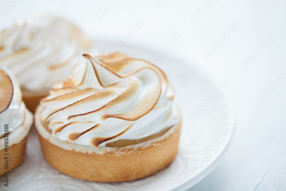 Delicious lemon tartlets with meringue on a white vintage plate. Sweet treat on a light blue background Delicious lemon tartlets with meringue on a white vintage plate. Sweet treat on a light blue background