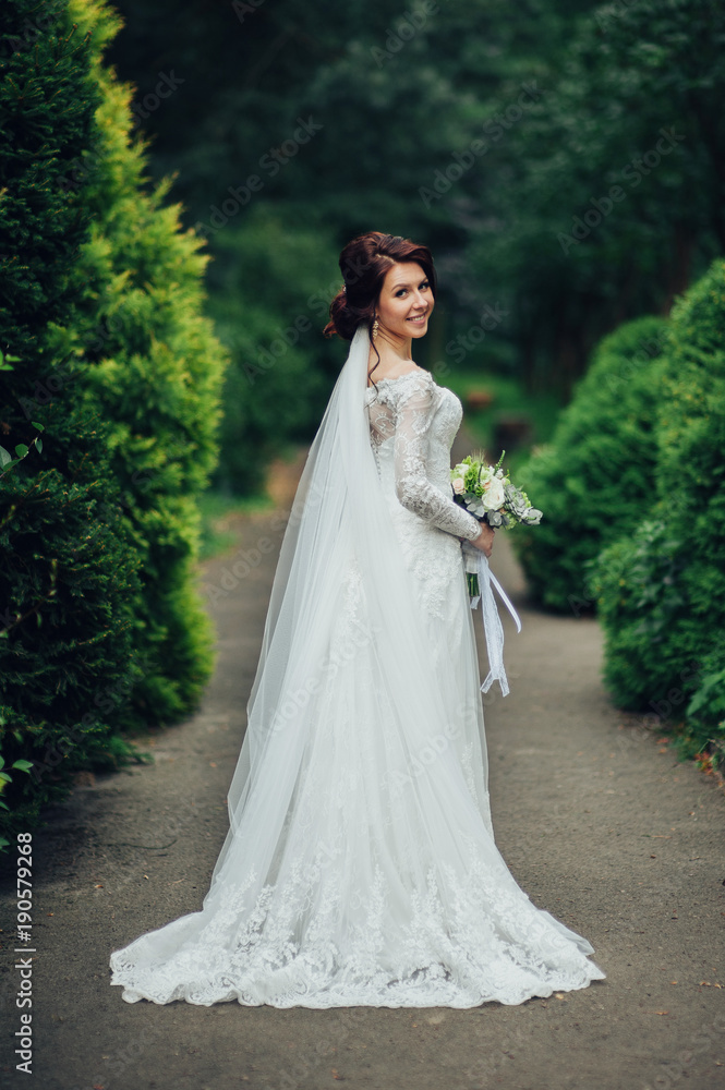 bride in a dress standing in a green garden and holding a weddin