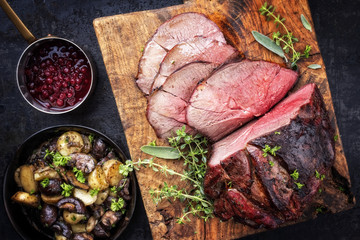 Barbecue dry aged haunch of venison with mushroom and potatoes as close-up on an old cutting board