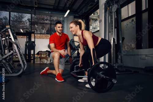 Girl exercising in the gym with assistance of personal trainer