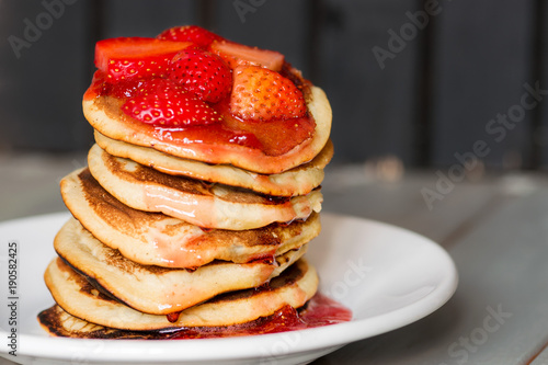 Delicious Strawberry Pancakes on a dark moody background, stunning breakfast with vibrant colors, white plate