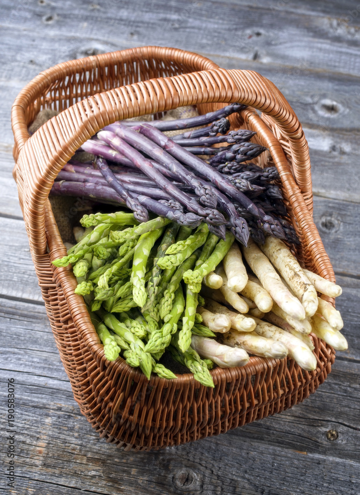 Fresh raw white, green and purple asparagus as top view in a basket