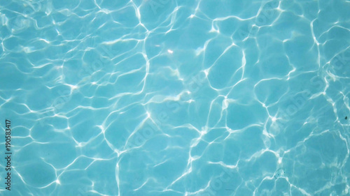 Water in swimming pool rippled water detail background. Water in swimming pool with sun reflection. Blue swimming pool rippled water detail