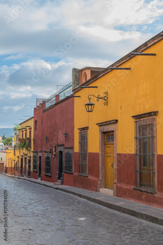 Colorful homes of red and yellow  lining a cobblestone street and stone sidewalk  in San Miguel de Allende