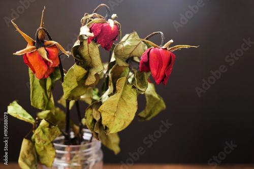 Dried roses in a vase on the wooden table on the black background. photo