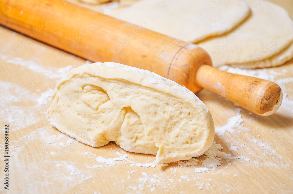 Rolled wheat dough and rolling pin on a wooden table