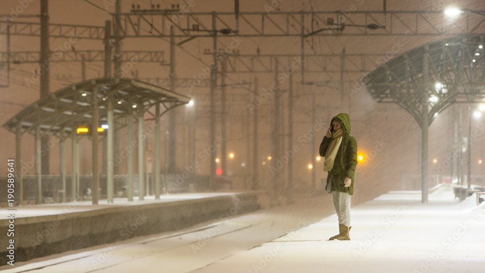 young woman on empty railway platform in blizzard waiting for a train / girl missed a train / woman is waiting for the train in bad weather and talking on the phone 