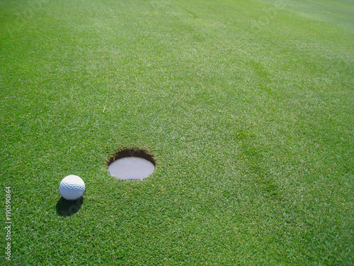 Golf ball close to the hole on a green lawn