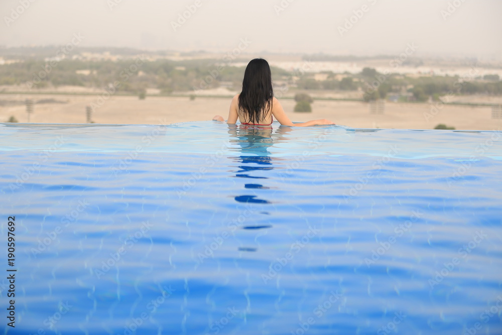 a back view of a asian woman in a swimming pool over the desert in Dubai UAE