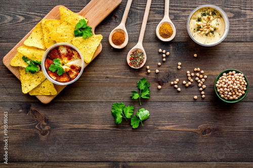 Hummus ready to eat. Bowl with dish among pieces of crispbread and spices on dark wooden background top view copy space