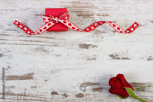 Wrapped gift with red ribbon and rose for Valentines Day, copy space for text on rustic board