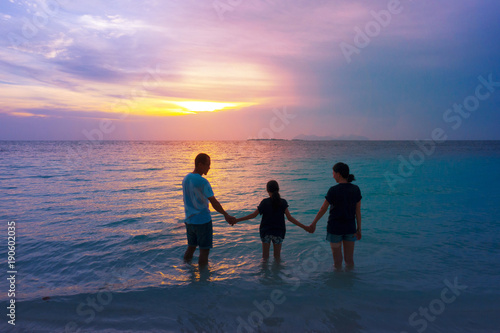 Happy Asian family in love on vacation and Happy valentines day. Dad mom and daughter holding hands and standing on tropical beach with dramatic sunset sky background. Relationship and family concept.