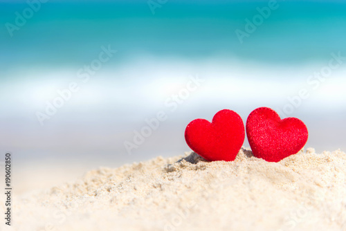 Valentine Concept. Two red hearts on the sand summer beach, blue background.