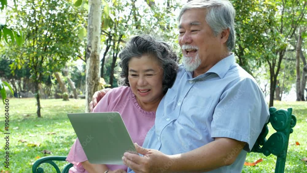 Asian couple elder people relax at park together. Elder people using laptop with happy emotion. People lifestyle concept Asian couple elder people relax at park together. Elder people using laptop with happy emotion. People lifestyle concept