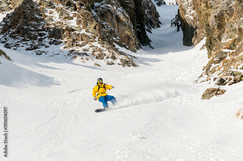 Fotografie A man a snowboarder freerider descends a backcountry at high speed from a slope