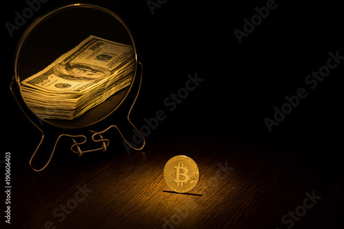 The Bitcoin Gold Coin is reflected in a mirror in the form of a pack of one hundred dollar bills, a business concept on a black background. photo