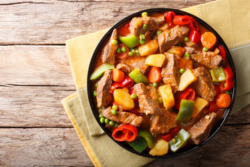 Asian food: Stewed beef with potatoes, peppers, peas, tomatoes and carrots close-up on the table. horizontal top view