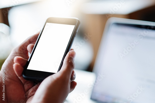 Mockup image of a man's hand holding white mobile phone with blank black desktop screen on thigh in cafe