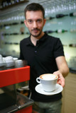 Men barista hold cup of coffee. Serving a client. Focus on beverage. Shallow depth of field.