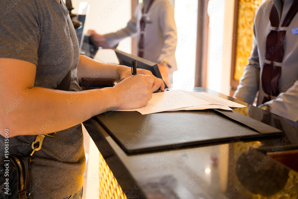 Fototapeta premium Goście płci męskiej meldują się w hotle, podpisując formularz w recepcji