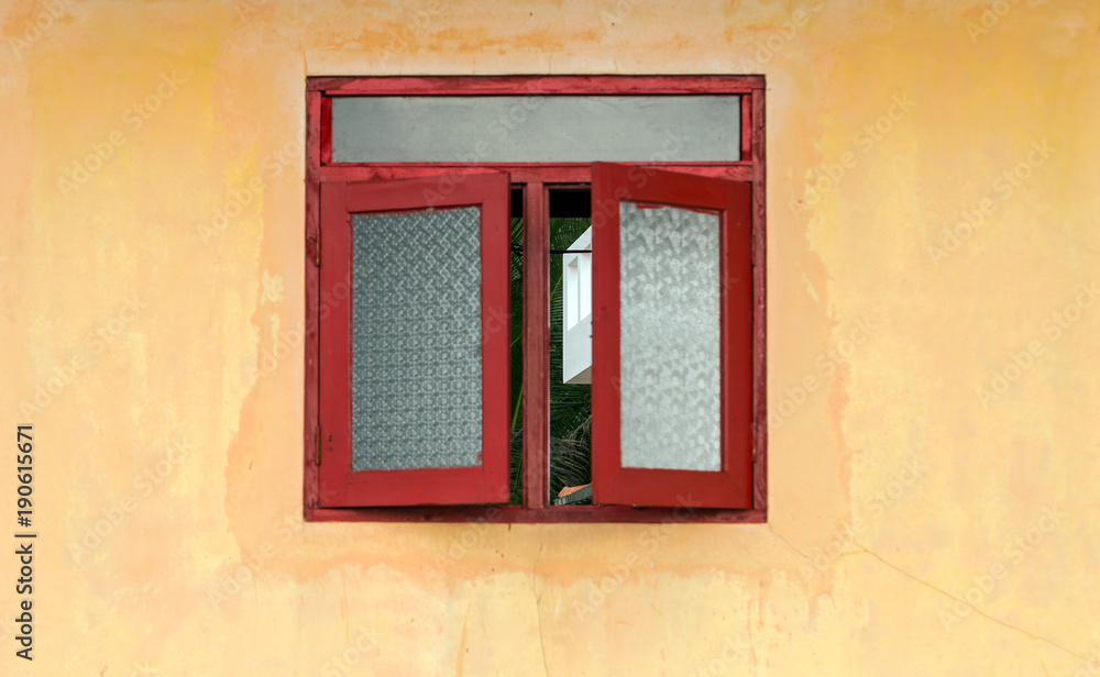 Red window with shutters in yellow house facade