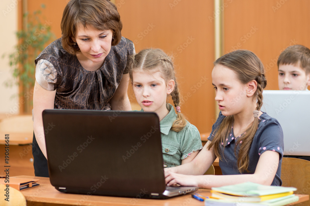 School kids and teacher at laptop in the classroom School kids and teacher at laptop in the classroom