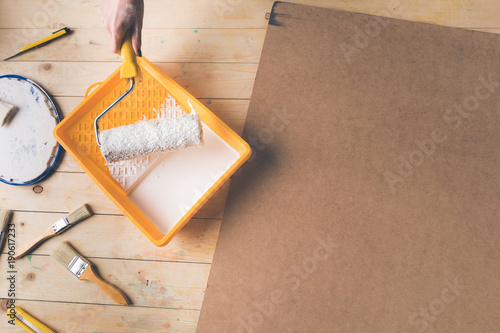 cropped image of woman putting paint roll brush in white paint
