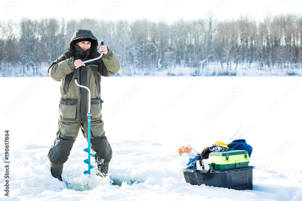 fisherman drills a hole in the ice. winter fishing in the background of a frozen lake