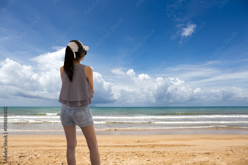 Asin woman in headphones standing on beach near the sea