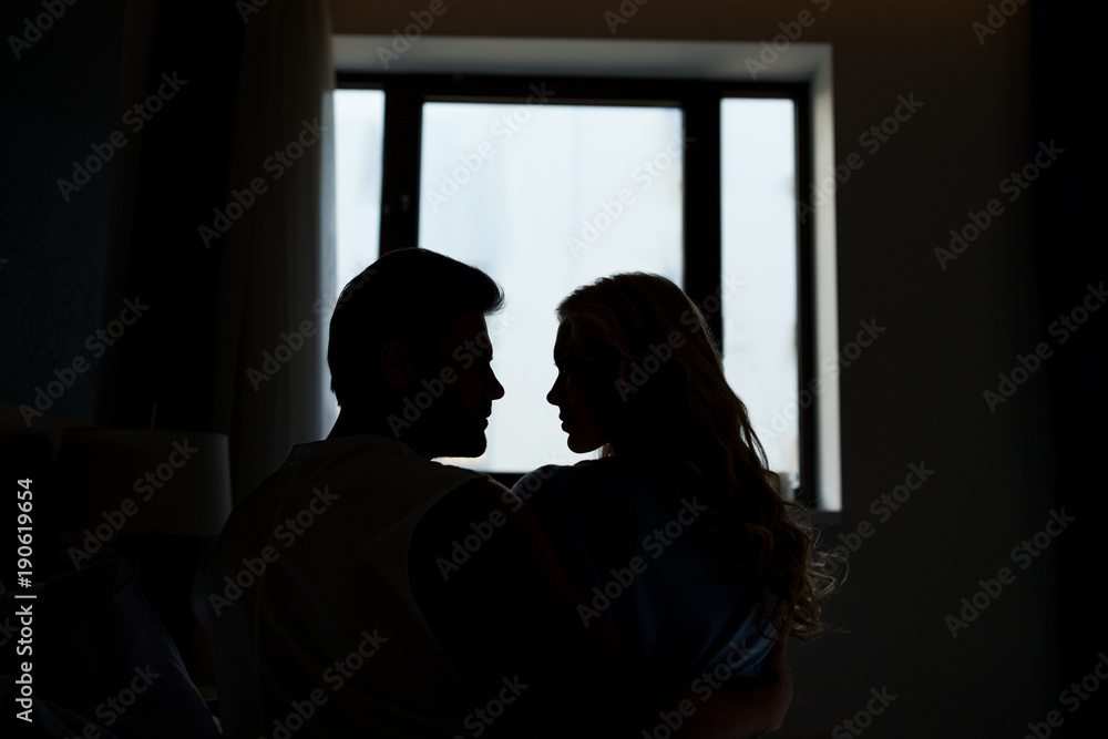 silhouettes of heterosexual couple looking at each other in dark room