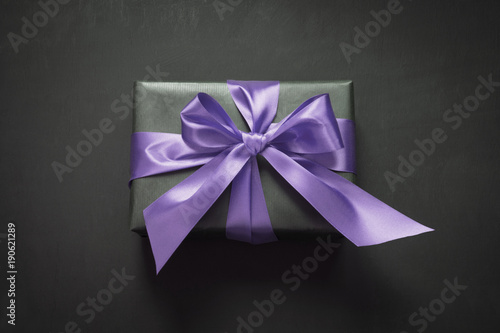 Gift box wrapped in black paper with ultra violet ribbon on black surface.