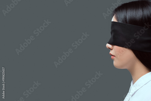 side view of young woman wearing black blindfold isolated on grey photo