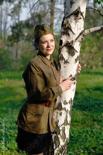 Pretty Soviet female soldier in uniform of World War II stands near the birch