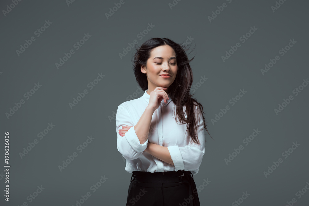 portrait of beautiful smiling asian girl standing with hand on chin isolated on grey portrait of beautiful smiling asian girl standing with hand on chin isolated on grey