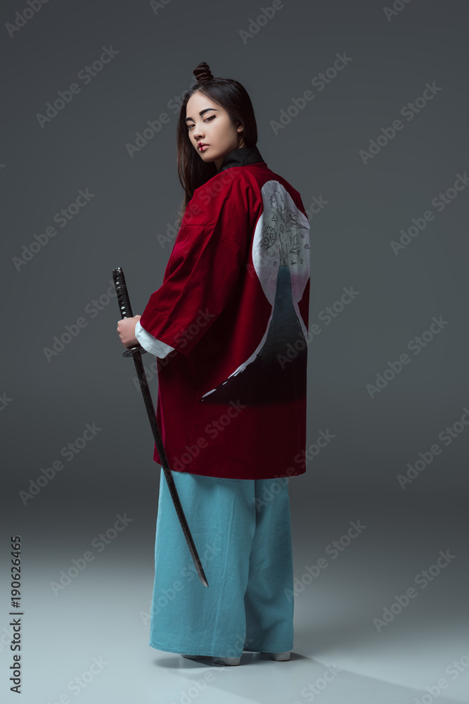 back view of woman in traditional japanese kimono holding katana and  looking at camera on grey Stock Photo | Adobe Stock