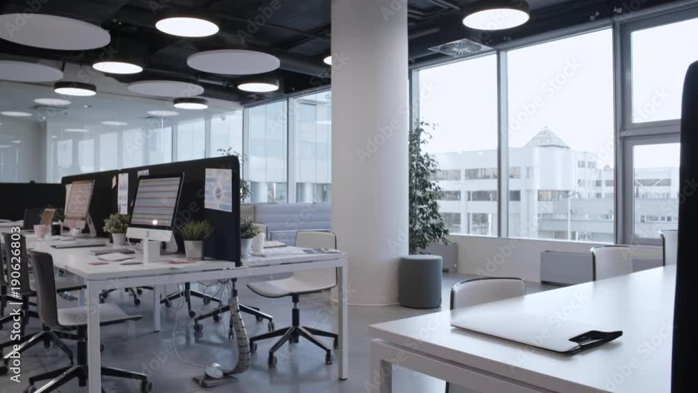 Tracking shot of empty open space office with stylish interior, panoramic window, comfortable furniture and modern computers