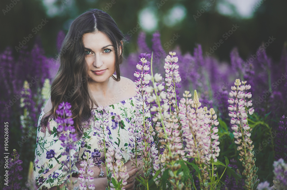 Beautiful young girl in ultra violet and white dress holding a bouquet of lupine at sunset on the field. The concept of nature and romance. The toning Beautiful young girl in ultra violet and white dress holding a bouquet of lupine at sunset on the field. The concept of nature and romance. The toning